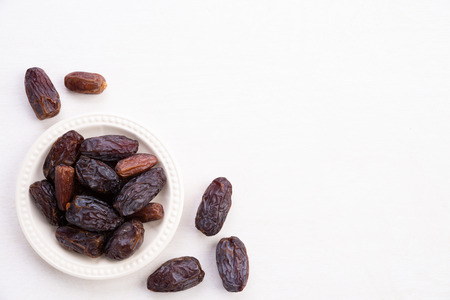 Ramadan food and drinks concept. Dates fruit and green Mint leaves in a bowl on a white wooden table background. Top view, Flat lay.の写真素材