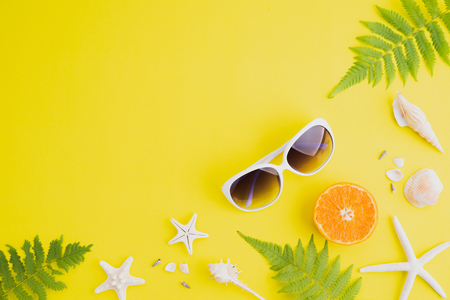 Beach accessories sunglasses, starfish, orange, fern leaves and sea shell on yellow background for summer holiday and vacation concept.の写真素材