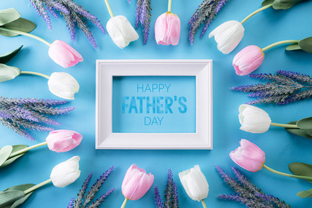 Happy fathers day concept. Top view of white pink tulip flowers and picture frame with Happy father's day text on bright blue pastel background. Flat lay.の写真素材
