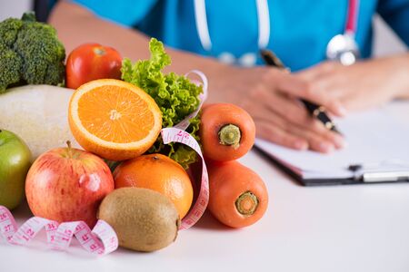 Healthy lifestyle, food and nutrition concept. Close up of fresh vegetables and fruits with stethoscope lying on doctor's desk.の写真素材