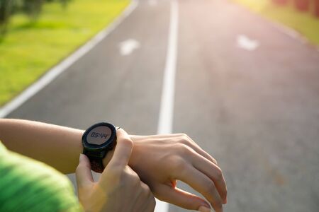 Young fitness woman runner setting up smart watch before running training during sunset. Outdoor exercise activities concept.の写真素材