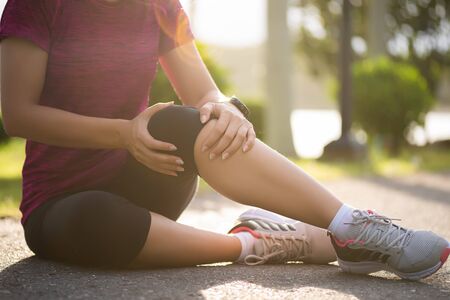 Young fitness woman runner feel pain on her knee in the park. Outdoor exercise activities concept.の写真素材
