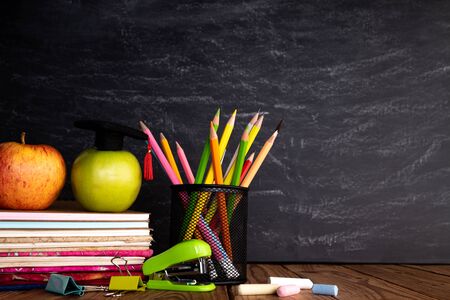 Education or back to school Concept. Colorful school supplies with books, color pencils, calculator, pen cutter clips and green apple on chalkboard background.の写真素材