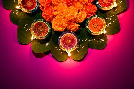 Happy Dussehra. Clay Diya lamps lit during Dussehra with yellow flowers, green leaf and rice on pink...