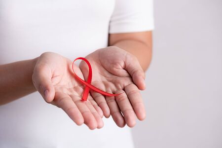 Closeup woman hand holding red ribbon HIV, world AIDS day awareness ribbon. Healthcare and medicine...
