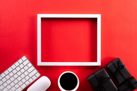 White picture frame with keyboard mouse coffee cup, gift box and Christmas tree decoration on red background. Online Shopping concept and black Friday composition.の写真素材