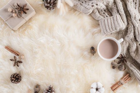 Autumn or winter composition. Gift box Coffee cup, cinnamon sticks, anise stars, beige sweater with knitted blanket on cream color gray fluffy background. Flat lay top view copy space.の写真素材