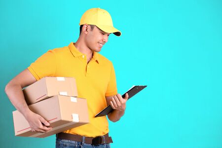 Happy delivery man in yellow polo shirt uniform holding parcel post box and checklist isolated over bright green pastel background. Smiling courier Delivery man.の写真素材