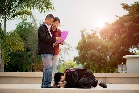 Graduation ceremony. Young female graduate giving graduation certificate to her parent at the university.の写真素材