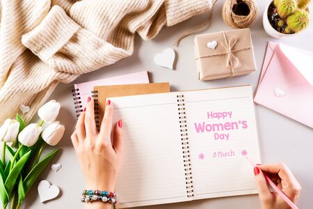 International Women's Day concept. Pink and white tulips with gift box and woman hand with pencil paper tag text on pink pastel background. Top view flat lay, March 8.の写真素材