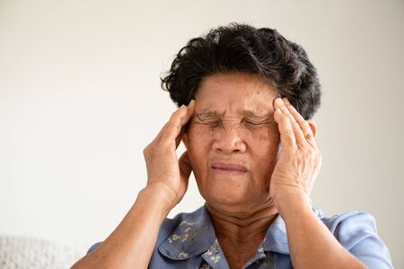 Asian old woman sitting on sofa and having a headache at home. Senior healthcare concept.の写真素材