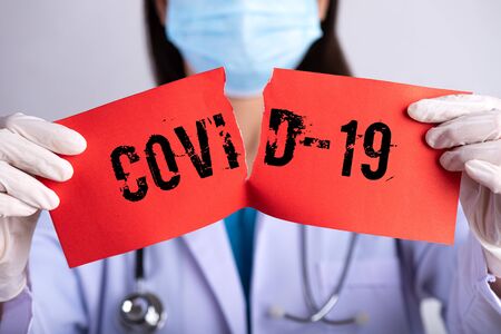 Female doctor wearing surgical mask, stethoscope and holding red torn paper with COVID-19 text. Healthcare and medical concept.の写真素材