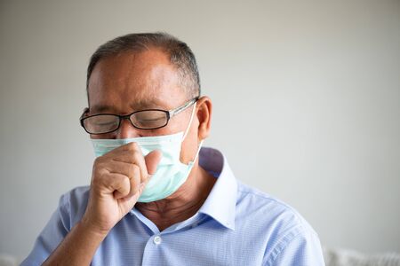 Asian old man wearing Protective face mask and cough, get ready for Coronavirus and pm 2.5 fighting, sitting on sofa at home. Senior healthcare concept.の写真素材