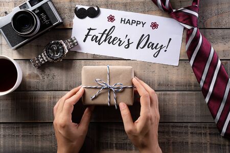 Happy Fathers Day background concept with coffee cup, decorated bowtie, necktie, eyeglasses, retro camera, gift box and mustache on old wooden background.の写真素材