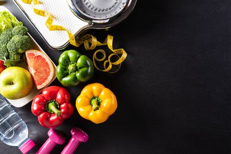 World health day, Healthcare and medical concept. Healthy food including fresh fruits, vegetables, weight scale, sports shoes, dumbells and measure tape on black background.の写真素材
