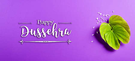 Happy Dussehra. Green leaf and rice on purple pastel background. Dussehra Indian Festival concept.