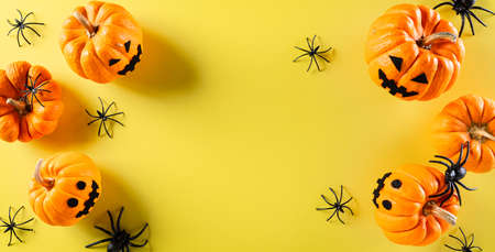 Top view of Halloween crafts, orange ghost pumpkin and black spider on pastel yellow background. Flat lay, top view with copy space.の写真素材