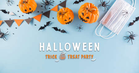 Halloween decorations made from pumpkin, paper bats and surgical face mask on pastel blue background. Flat lay, top view of Halloween celebration during covid-19 pandemic situation.の写真素材
