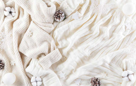 Winter cozy background with cotton flower, snowflake, pine cone and christmas ball on warm sweater...