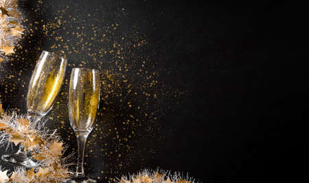 Christmas and New Year holidays background concept made from champagne glasses with golden glitter on black wooden background.の写真素材