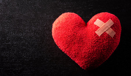 Close-up of cushioned plaster strip on hand made red heart with dark background. Broken heart, Love,...