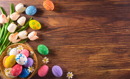 Happy easter! Colourful of Easter eggs in the nest with flower on dark wooden background. Greetings...
