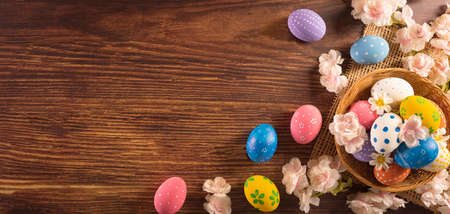 Happy easter! Colourful of Easter eggs in the nest with flower on dark wooden background. Greetings and presents for Easter Day celebrate time. Flat lay ,top view.の写真素材