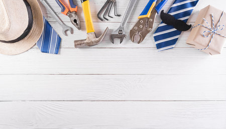 Happy Father's Day decoration with beautiful tie with mustache, hand tools, glasses, gift box and hat on white wooden background.の写真素材