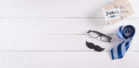 Happy Father's Day decoration with blue tie with mustache, glasses, gift box and greeting card on white wooden background.の写真素材