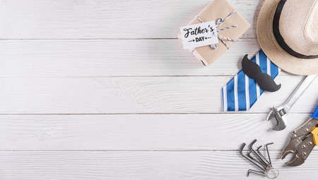 Happy Father's Day decoration with beautiful tie with mustache, hand tools, glasses, gift box and hat on white wooden background.の写真素材