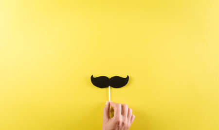 Happy Father's Day background concept with hand holding black mustache on pastel yellow background.の写真素材