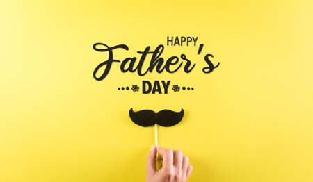 Happy Father's Day background concept with hand holding black mustache with the text on pastel yellow background.の写真素材