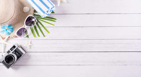 Summer holiday, travel and vacation concept. Sunglasses, starfish, beach hat, flip flop, retro camera and seashell on white wooden background.の写真素材