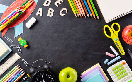 Education or back to school Concept. Top view of Colorful school supplies with books, color pencils, calculator, pen, cutter, clips and green apple on backboard background. Flat lay.の写真素材