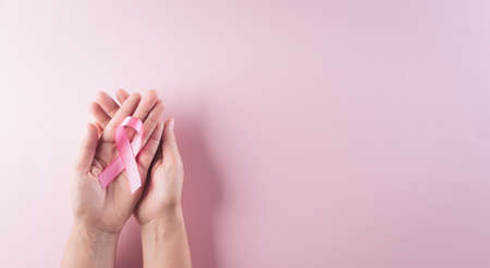 Hands holding pink ribbon, Breast cancer awareness, symbolic bow color raising awareness on women's breast tumor. Healthcare and medical concept.の写真素材