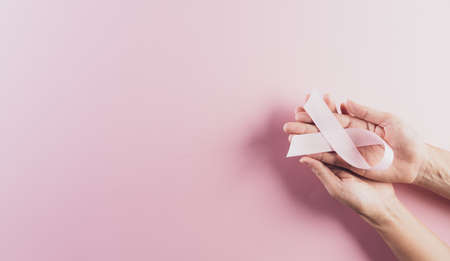 Hands holding pink ribbons, Breast cancer awareness, symbolic bow color raising awareness on women's breast tumor. Healthcare and medical concept.の写真素材