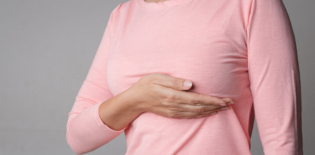 Woman hand checking lumps on her breast for signs of breast cancer on gray background. Healthcare concept.の写真素材