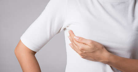 Woman hand checking lumps on her breast for signs of breast cancer on gray background. Healthcare concept.の写真素材