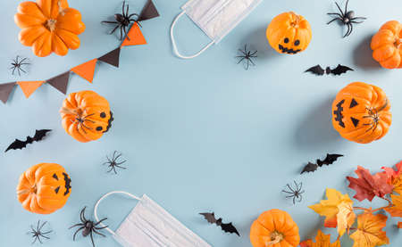 Halloween decorations made from pumpkin, paper bats and surgical face mask on pastel blue background. Flat lay, top view of Halloween celebration during covid-19 pandemic situation.の写真素材