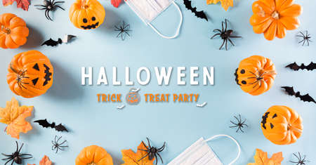 Halloween decorations made from pumpkin, paper bats and surgical face mask on pastel blue background. Flat lay, top view of Halloween celebration during pandemic situation.の写真素材