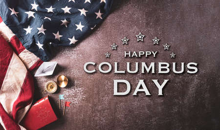 Happy Columbus Day concept. Vintage American flag, compass, paper boat, rope with the text on dark stone background.の写真素材