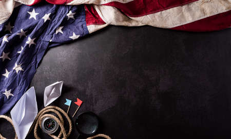 Happy Columbus Day concept. Vintage American flag, compass, paper boat, rope on dark stone background.  Flat lay, top view with copy space.の写真素材