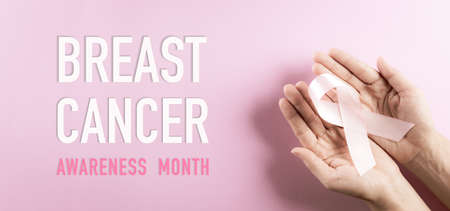 Hands holding pink ribbon, Breast cancer awareness, symbolic bow color raising awareness on women's breast tumor. Healthcare, medicine and breast cancer awareness concept.の写真素材