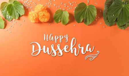 Happy Dussehra. Yellow flowers, green leaf and rice on orange background. Dussehra Indian Festival concept.の写真素材