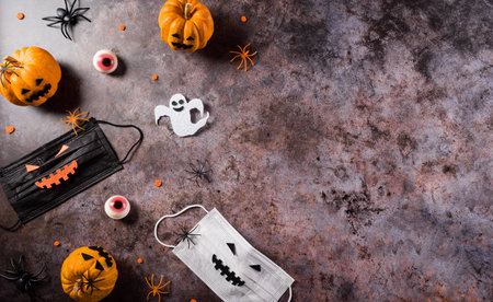 Halloween decorations made from pumpkin, paper bats,medical mask and black spider on dark stone background. Flat lay, top view with copy space for text.の写真素材