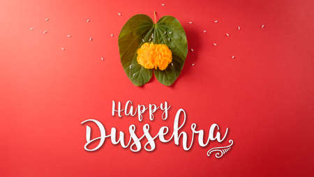 Happy Dussehra. Yellow flowers, green leaf and rice on red background. Dussehra Indian Festival concept.の写真素材