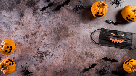Halloween decorations made from pumpkin, paper bats,medical mask and black spider on dark stone background. Flat lay, top view with copy space for text.の写真素材