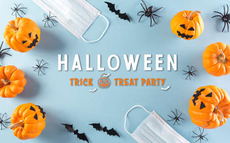 Halloween decorations made from pumpkin, paper bats and surgical face mask on pastel blue background. Flat lay, top view of Halloween celebration during pandemic situation.の写真素材