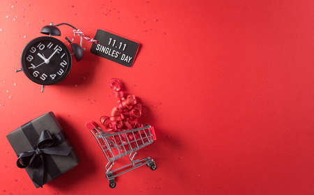 Online shopping of China, 11.11 singles day sale concept. Top view of shopping cart, black christmas gift boxes with sale card on red background with copy space.の写真素材
