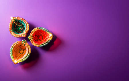 Happy Diwali - Clay Diya lamps lit during Dipavali, Hindu festival of lights celebration. Colorful traditional oil lamp diya on purple backgroundの写真素材